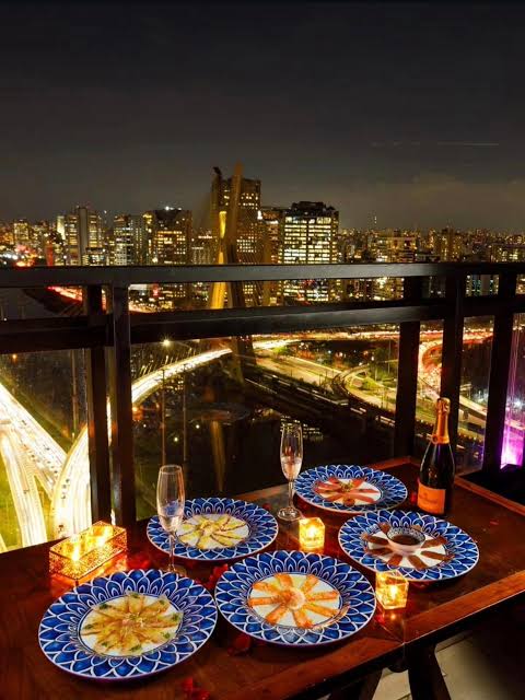 Mesa na varanda com espumante e pratos servidos sobre a ponte iluminada